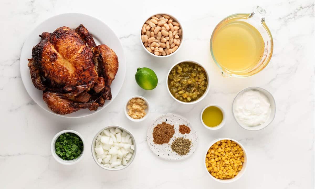 ingredients for white chicken chili: whole rotisserie chicken, chicken broth, white beans, corn, onion, garlic, green chilies, seasonings, a lime, and cilantro