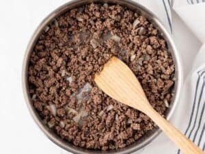 cooked ground beef in a skillet with a wooden spoon