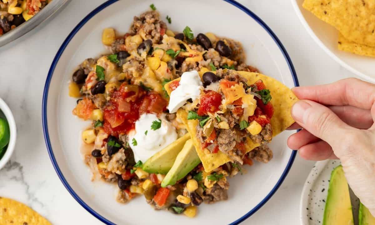 a hand grabbing taco meat with a tortilla chip
