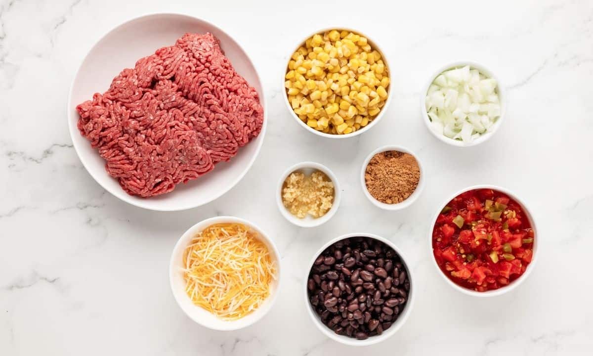 ingredients for taco skillet: ground meat, shredded cheese, beans, tomato, onion, garlic, and seasonings