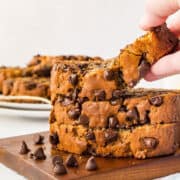 front view of a few slices of brown butter banana bread with chocolate chips on top of each other with a hand lifting one slice