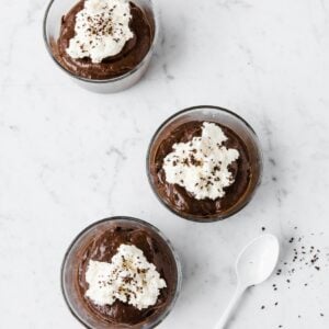 overhead view of chocolate avocado mousse in serving cups topped with whipped cream and cocoa shavings