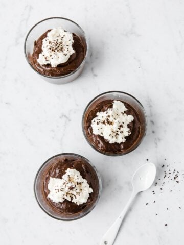 overhead view of chocolate avocado mousse in serving cups topped with whipped cream and cocoa shavings