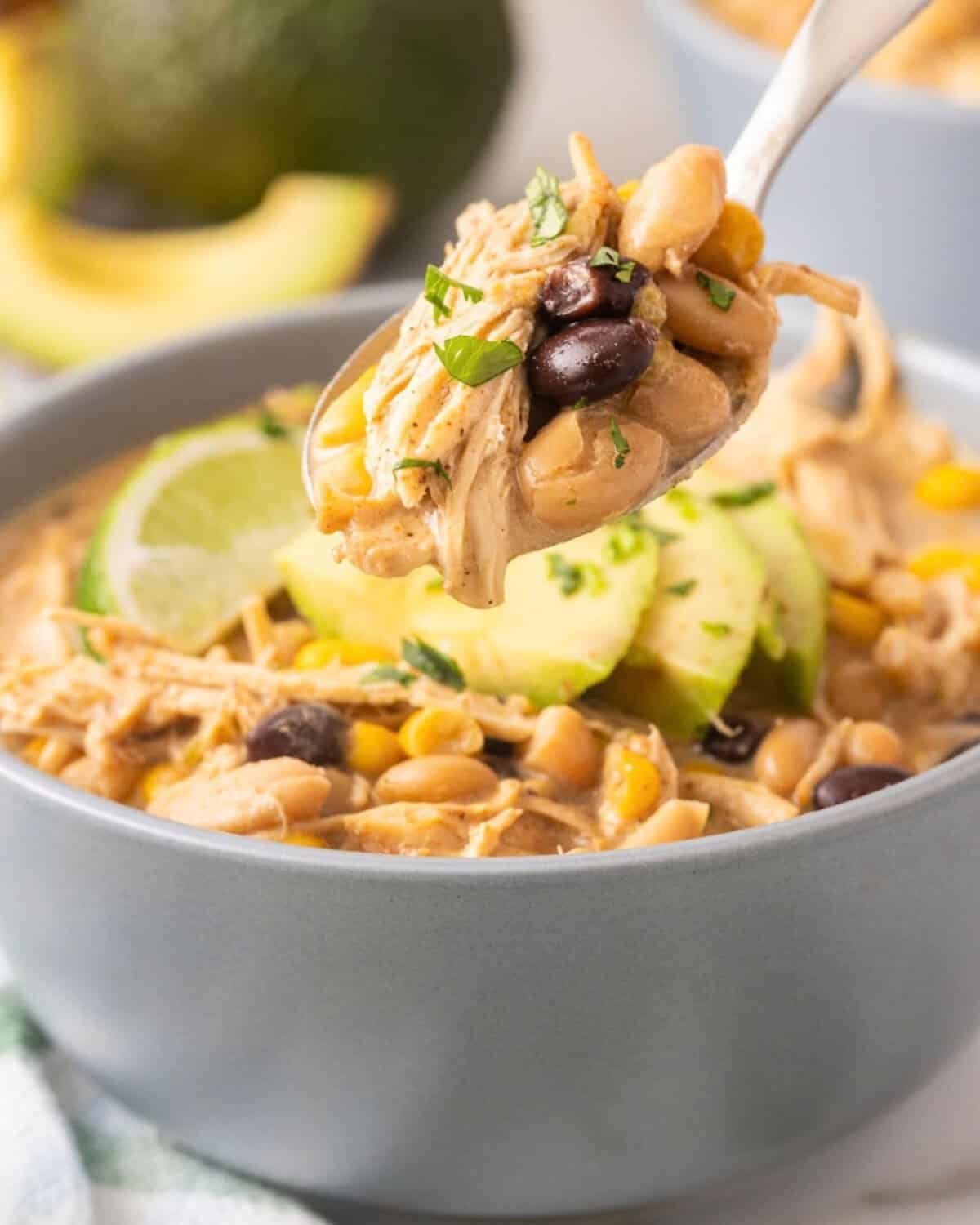 close up view of a creamy bowl of white chicken chili and a spoon picking up a spoonful