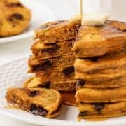 a stack of pumpkin protein pancakes topped with butter, drizzled with syrup, and with a wedge cut out