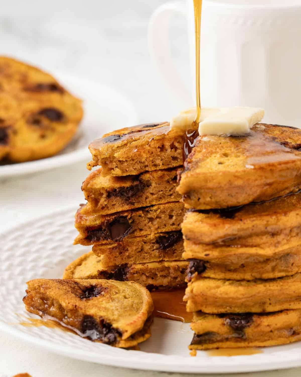 a stack of pumpkin protein pancakes topped with butter, drizzled with syrup, and with a wedge cut out