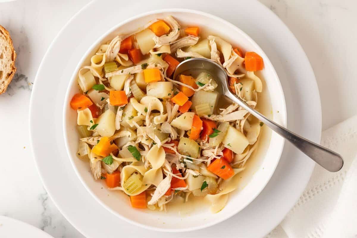 overhead view of a bowl of chicken noodle soup with potatoes