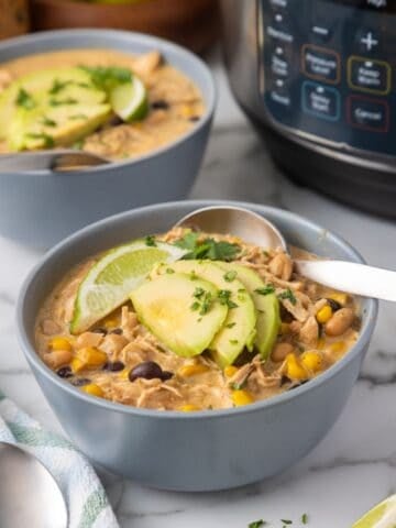 front view of a bowl of white chicken chili made in the instant pot. another bowl behind it and the appliance is visible